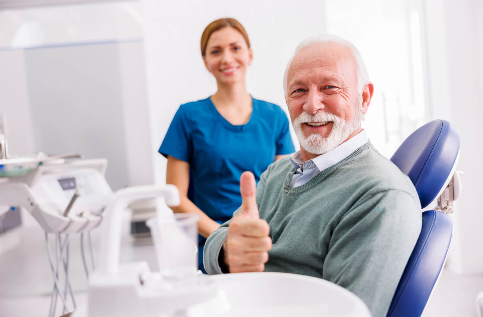 A senior man smiling with his female dentist, giving a thumbs up while in the dental chair