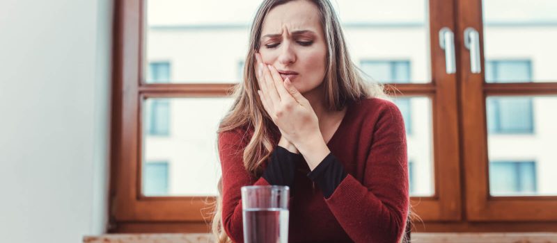 A woman is applying pressure to her cheek as she experiences toothache and is resorting to an over-the-counter pain reliever to ease the discomfort.