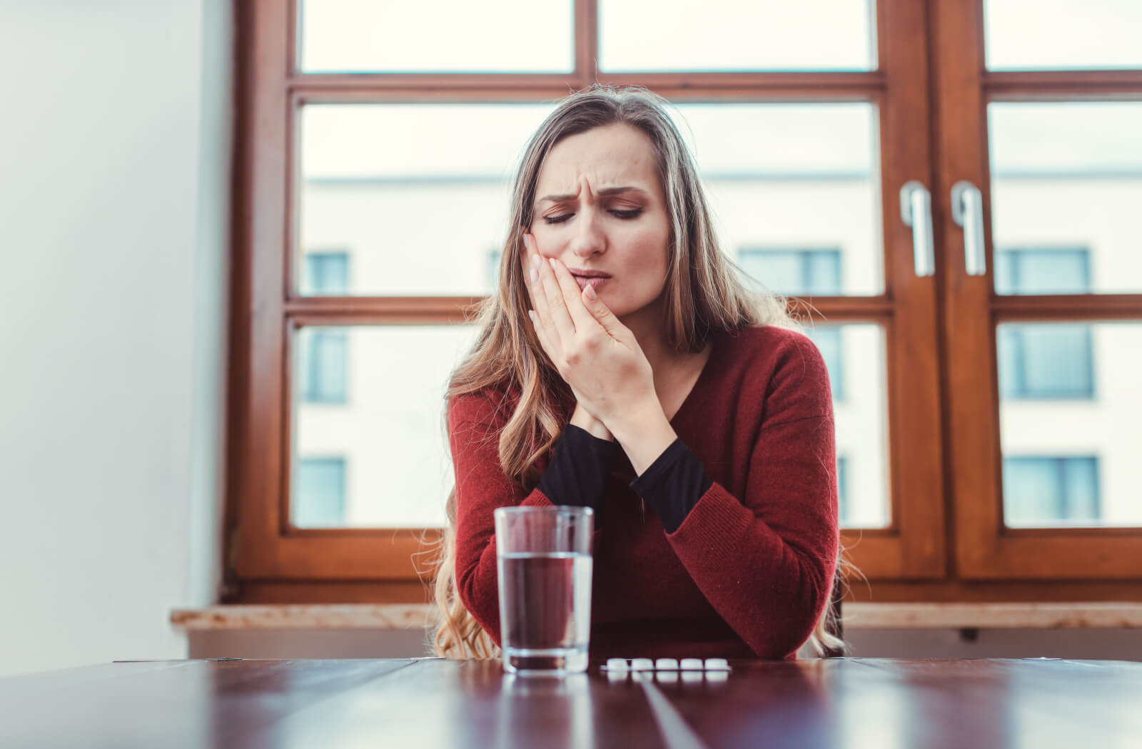 A woman is applying pressure to her cheek as she experiences toothache and is resorting to an over-the-counter pain reliever to ease the discomfort.