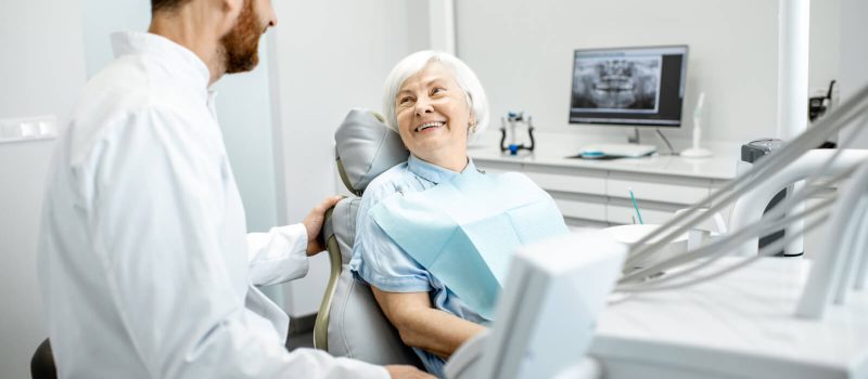 A senior woman sitting in a dental chair and smiling at her male dentist