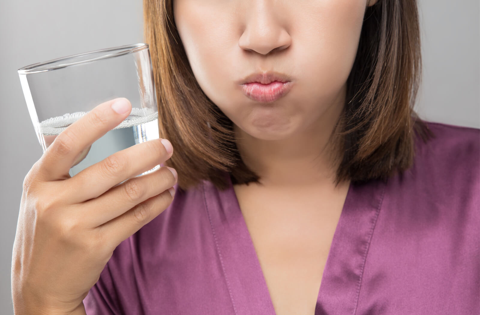 A close-up of a woman holding a glass of saltwater intended for gargling following a tooth extraction.
